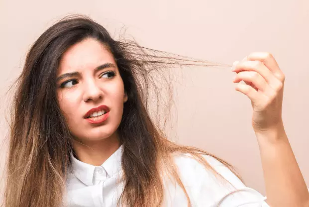Young woman looking at her rough and damaged hair